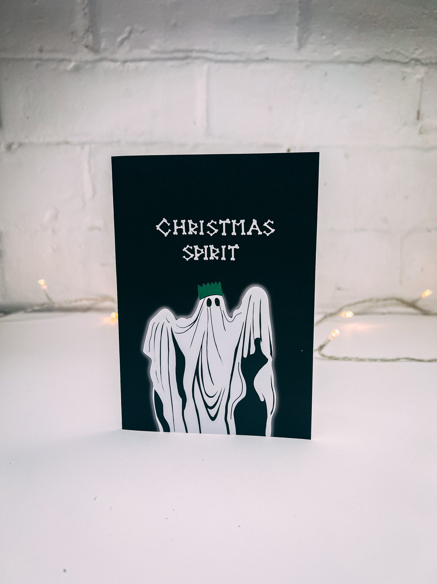 Wayward - black christmas card writing in bones with Christmas spirit, underneath illustration of ghost with a christmas hat