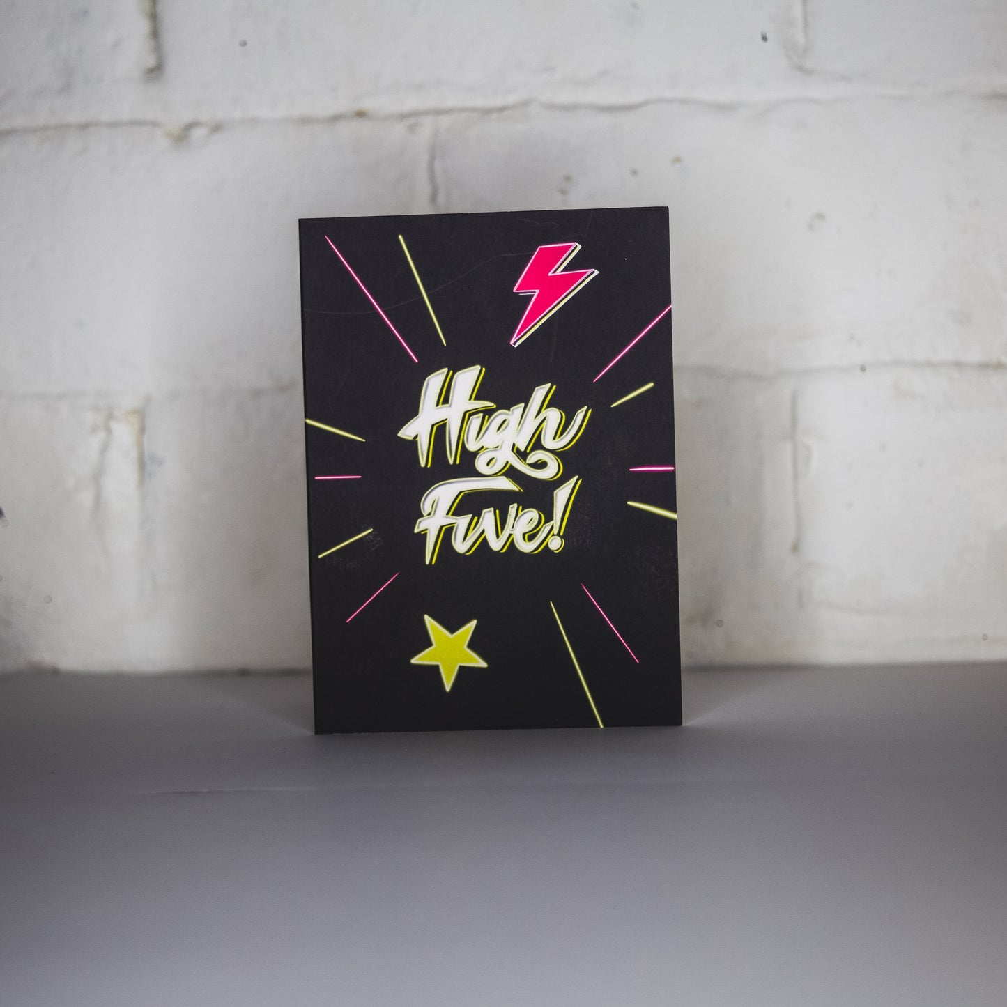 Black Greetings Card With White and Yellow Neon High Five Writing with Lightening Bolt and Star Design by Wayward