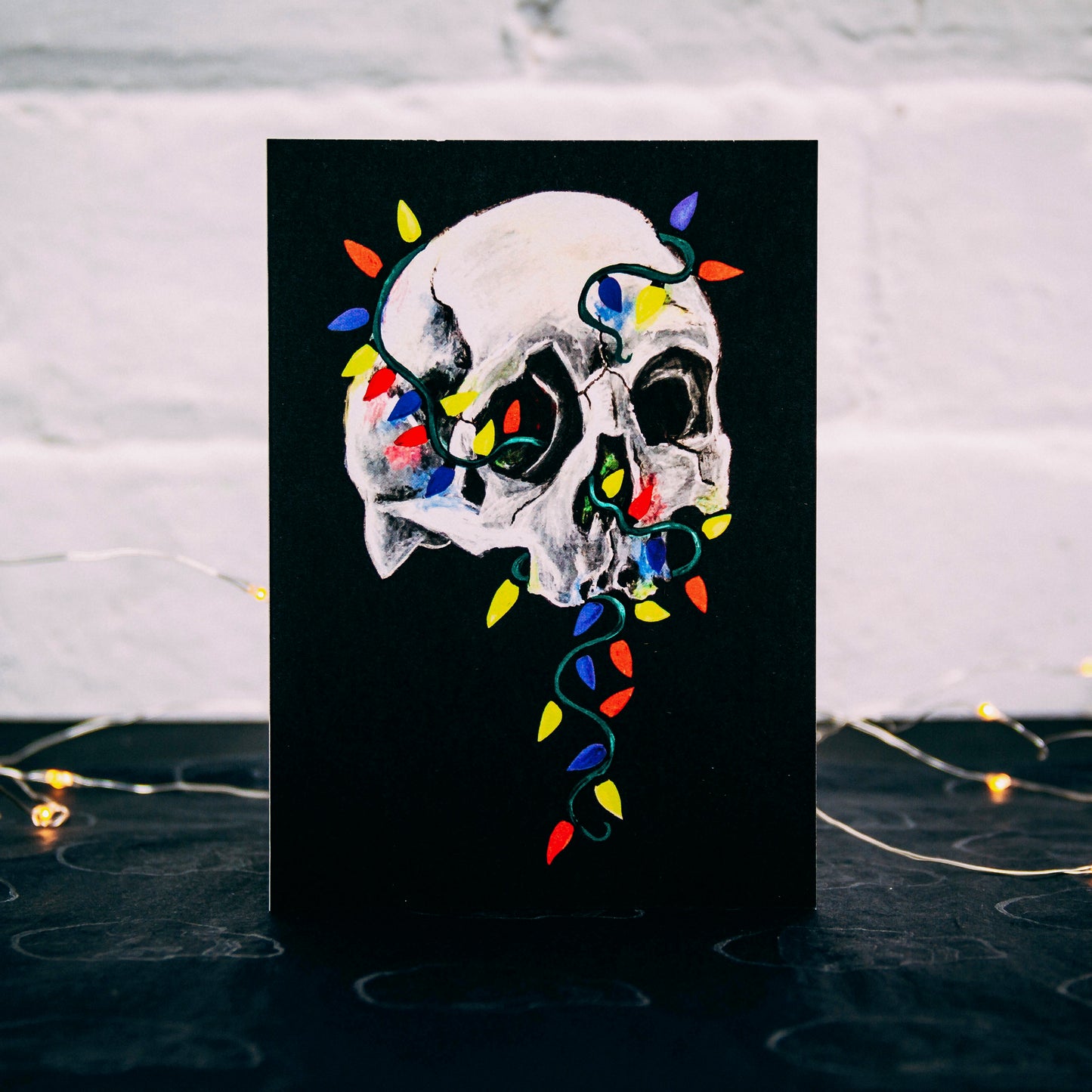 Skull with colorful christmas lights wrapped around on black background. Christmas card by Wayward