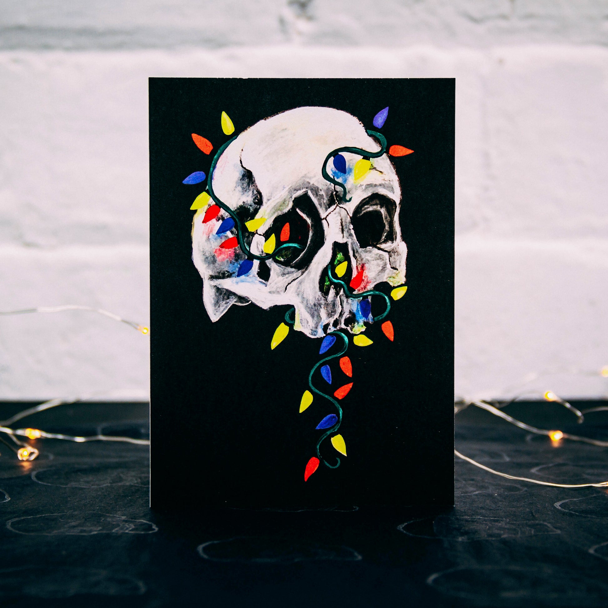 Skull with colorful christmas lights wrapped around on black background. Christmas card by Wayward