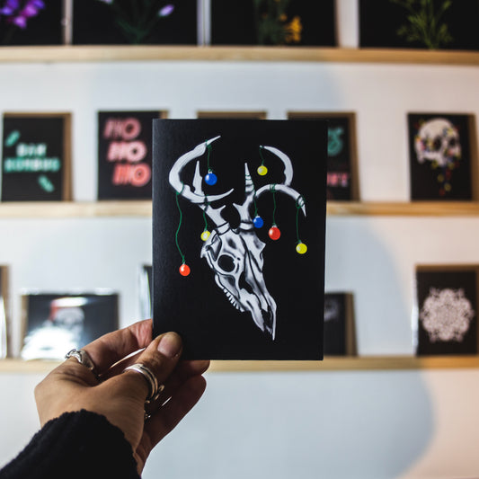 Deer skull with baubles on antlers on black background christmas card by wayward