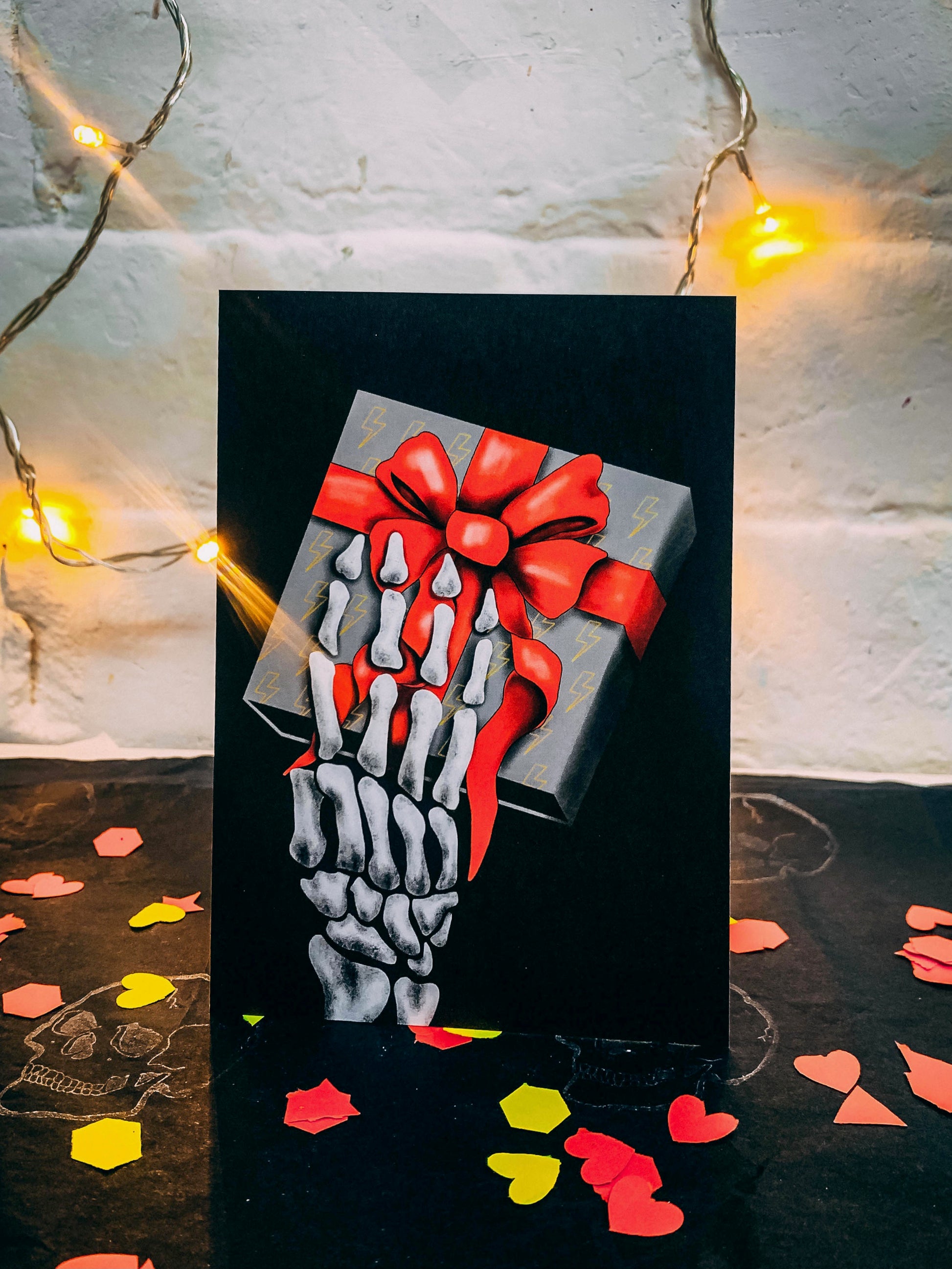 Black A6 greetings cards with skeleton hand holding a grey box with red ribbon by Wayward