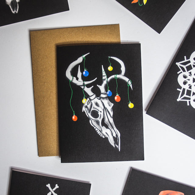 Deer skull with baubles on antlers on black background christmas card by wayward