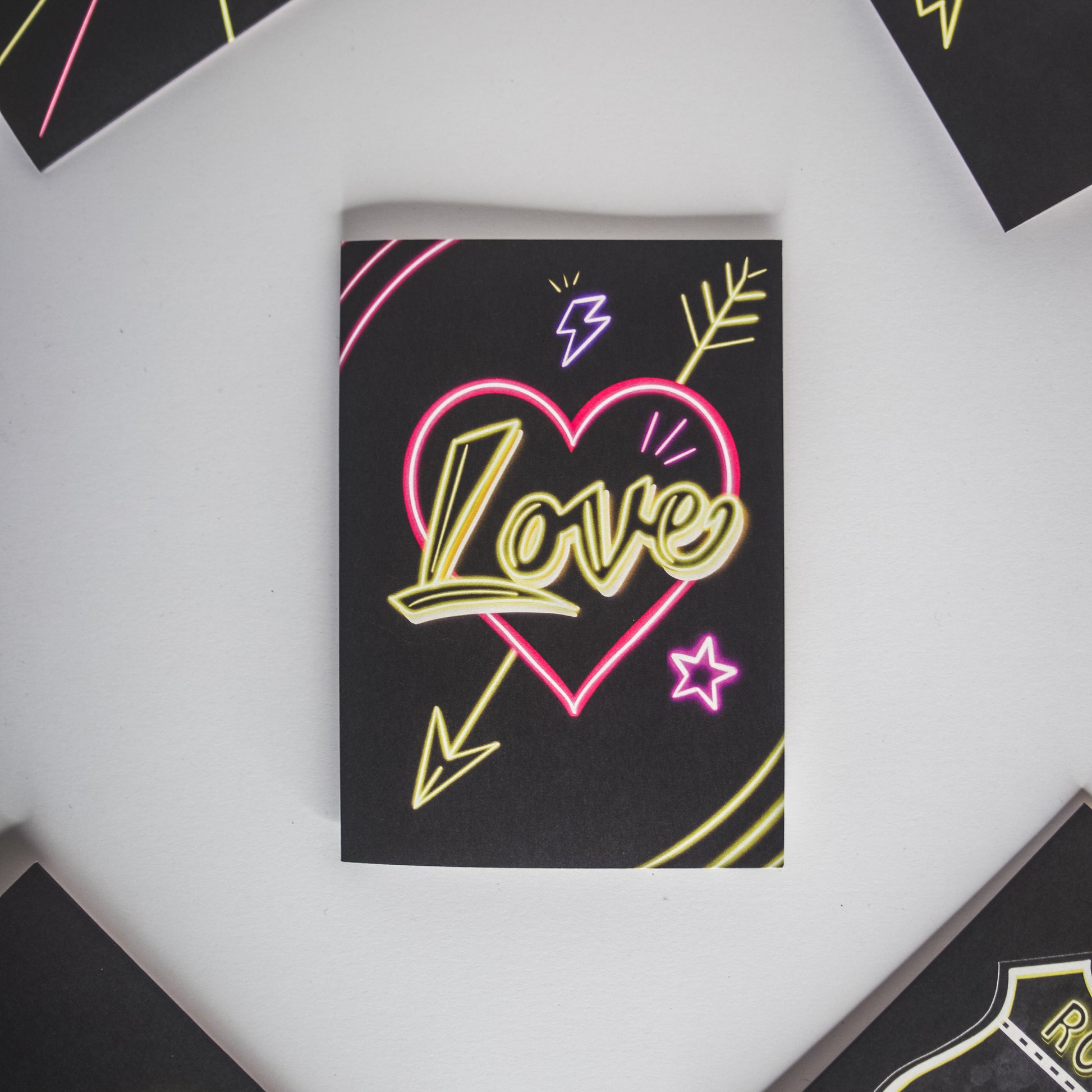 Black Greetings Card with Yellow Love Neon Writing in Pink Heart by Wayward
