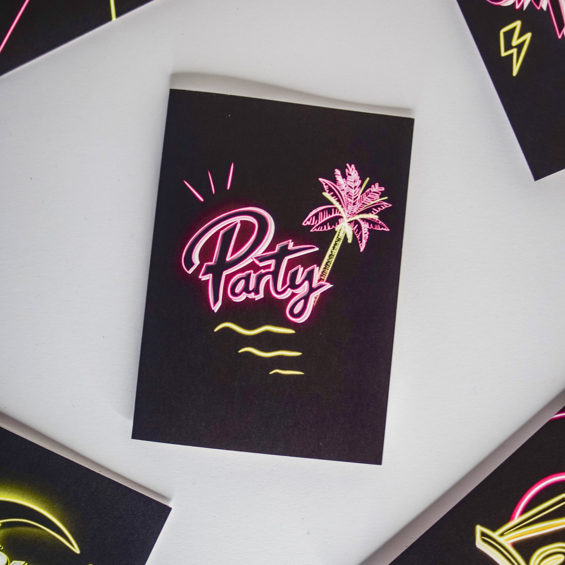 Black greetings card with party written in pink neon with a palm tree by wayward