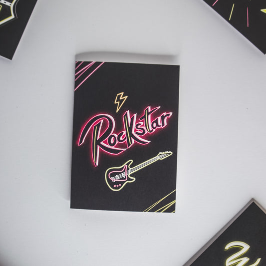 Black Greetings Card with Rockstar written in pink neon with a guitar
