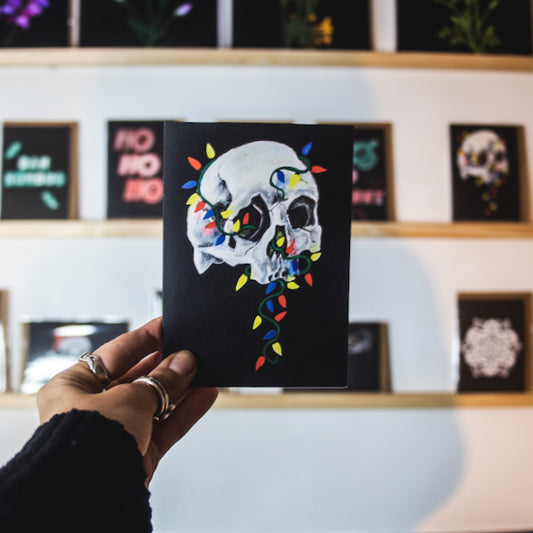 Skull with colorful christmas lights wrapped around on black background. Christmas card by Wayward