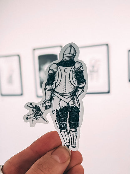Hand holding a sticker of a knight  in front of a wall with framed pictures.