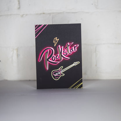 Black Greetings Card with Rockstar written in pink neon with a guitar 