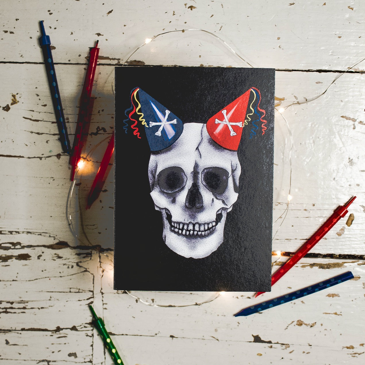 Flatlay of Black Birthday Card with Illustration of skull wearing party hats as horns 