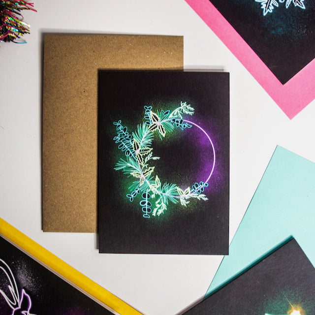 Christmas card by Wayward. Glowing green and purple neon wreath on black background