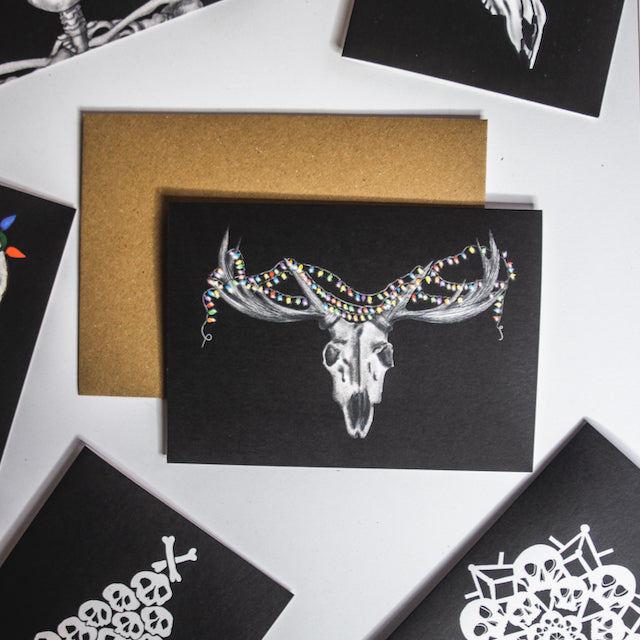 Deer skull with colorful christmas lights wrapped round horns on black background. Christmas card by wayward