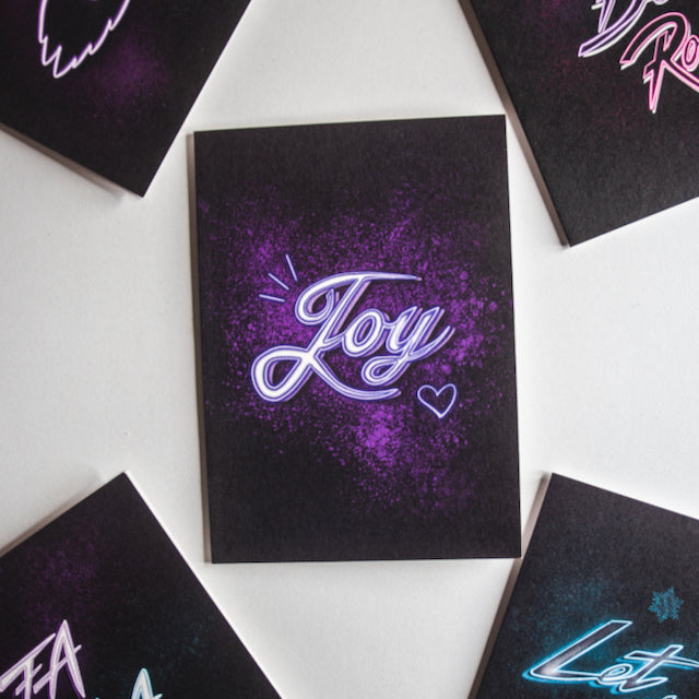 Purple Joy neon writing in purple splatter on black background christmas card by wayward