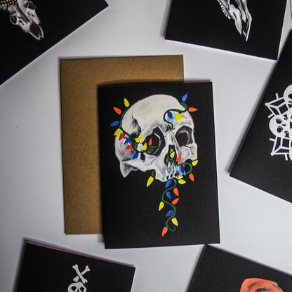 Skull with colorful christmas lights wrapped around on black background. Christmas card by Wayward