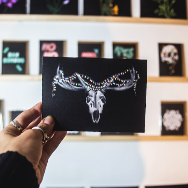 Deer skull with colorful christmas lights wrapped round horns on black background. Christmas card by wayward